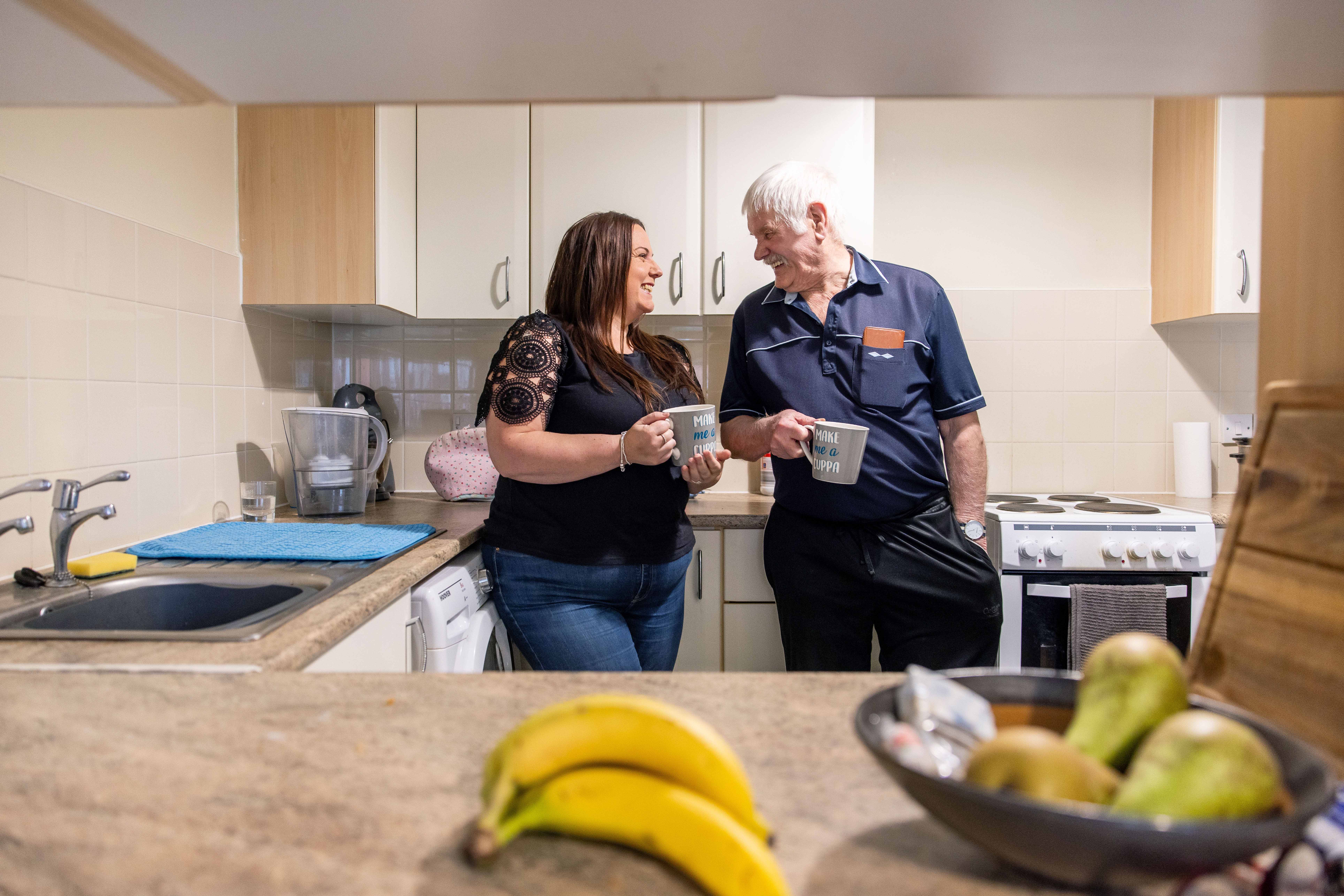 Woman and man standing in kitchen with a drink in their hand looking at each other and smiling