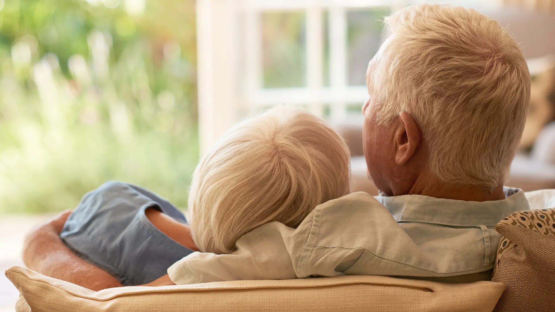 Older Couple Cuddling On Sofa Backs To Camera