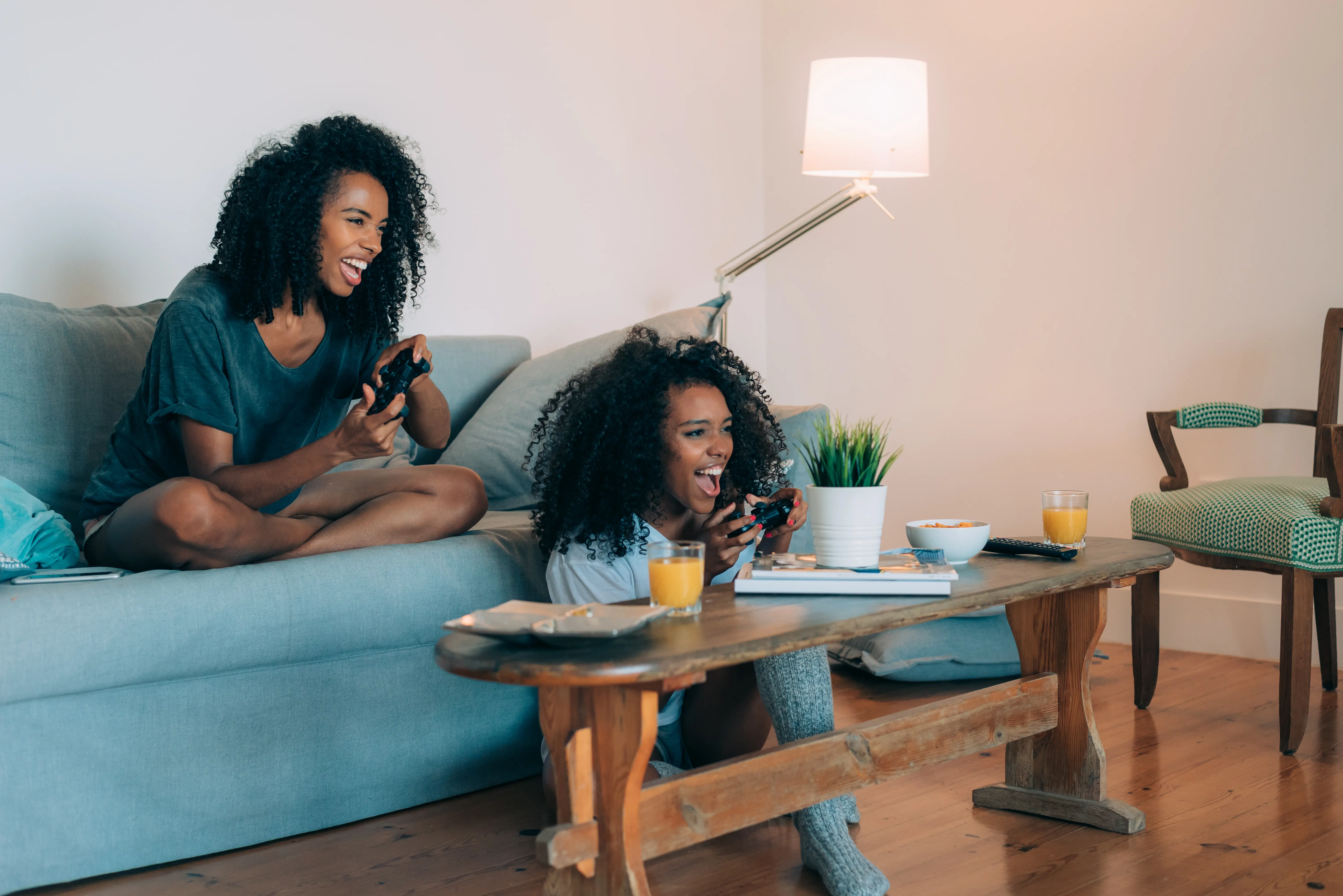 Two Women At Home Playing Video Games Sitting On Sofa