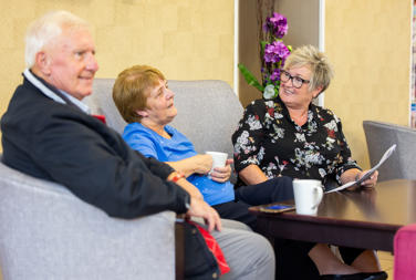 An older couple sat down talking to a member of staff over a cup of coffee